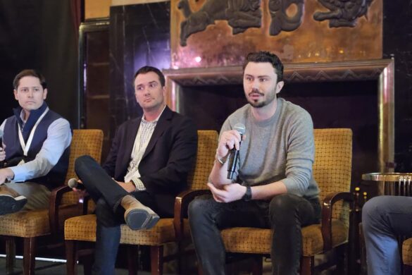 Men in business casual attire sit in yellow armchairs as they address an audience at the BuiltWorlds 2025 Venture West Conference.